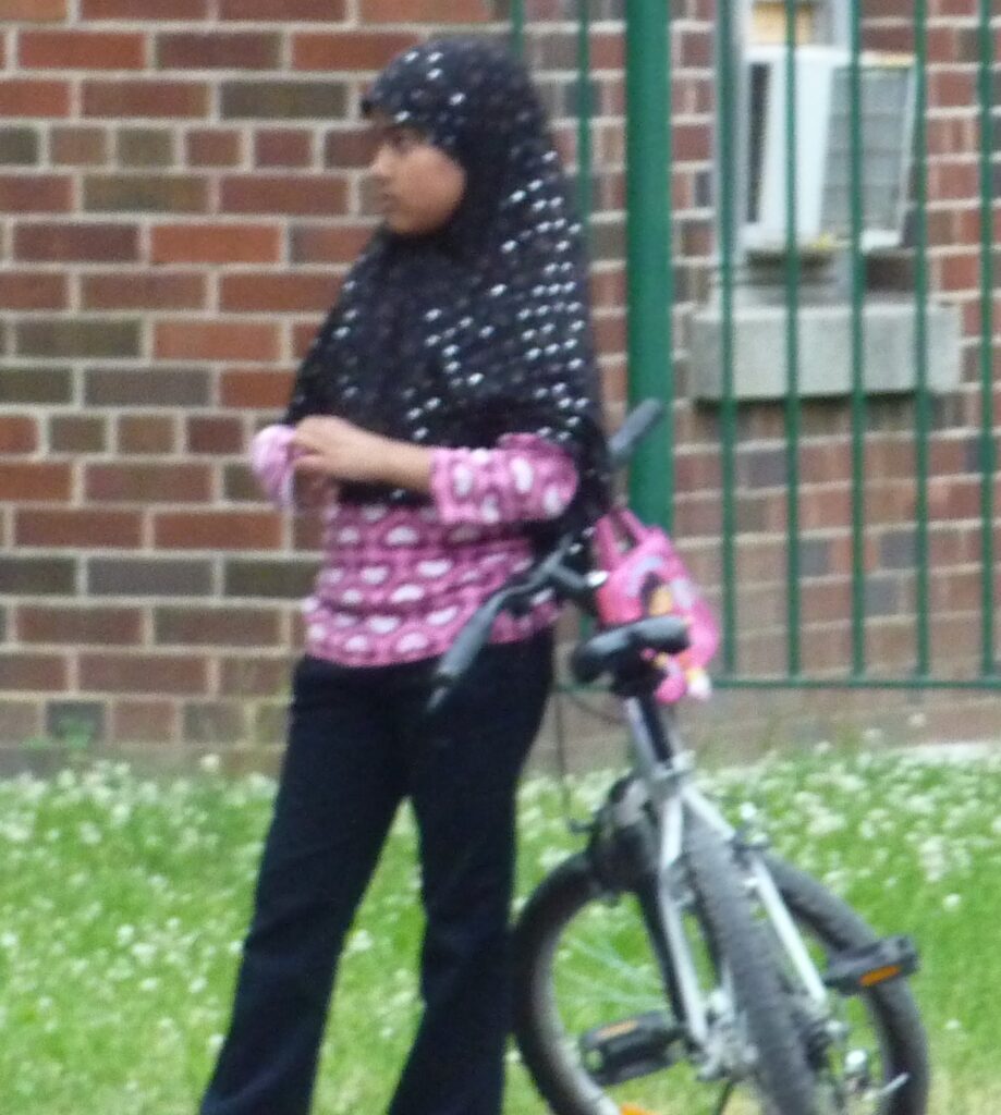 Muslim female ten years old standing beside her bike. She wears a full hijab. This girls seems at the age of 9 to be impregnated