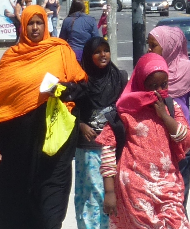 Mother wearing an orange hijab is walking with her three daughters. They are  eight to twelve years old. They all wear a full covering hijab. These girls cannot marry non Muslims