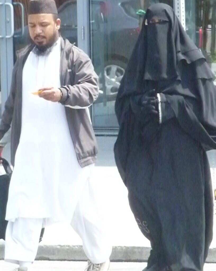 Orthodox Muslim couple man wearing white gown woman wears complete black even gloves small slit for vision 