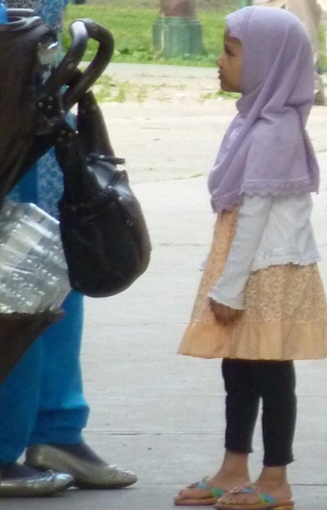 Small girl 5 years old. wears a pink Muslim head scarf covers her shoulders. her face is visible