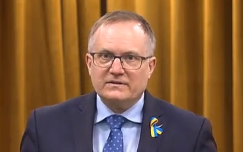 Man 50 years old glasses  blue yellow lapel blue jacket shirt is light blue. tie with blue with very pale blue dots Promote truth cancel falsehood 